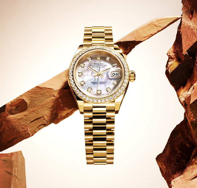 Rolex gold Lady Datejust watch with link bracelet and diamond detail around dial, rocks in background