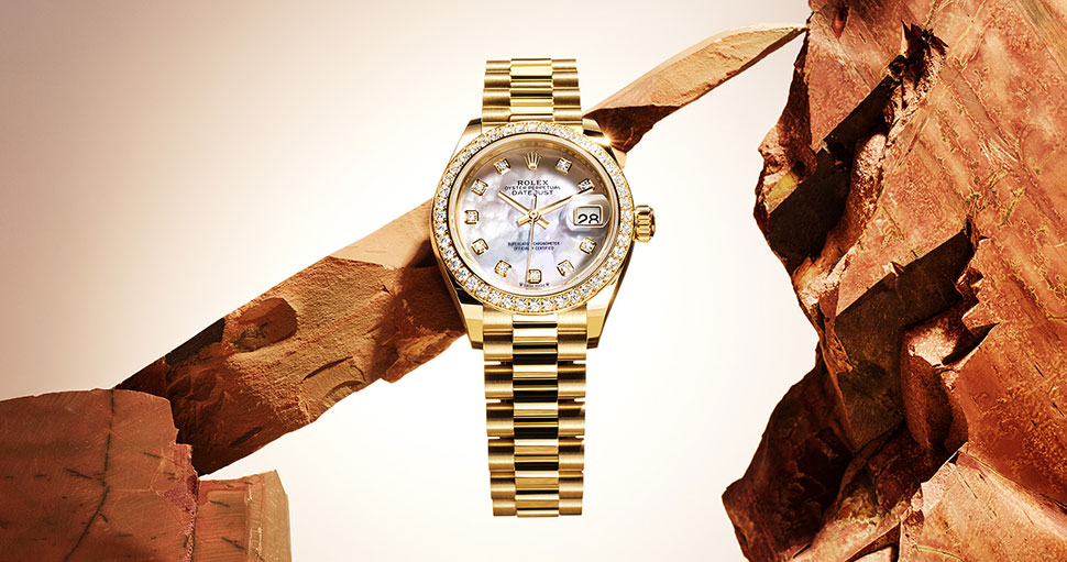 Rolex gold Lady Datejust watch with link bracelet and diamond detail around dial, rocks in background