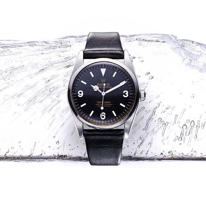 Rolex watch with black dial and black leather strap on ice