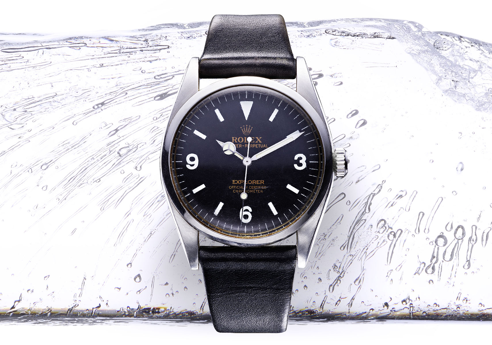Rolex watch with black dial and black leather strap on ice